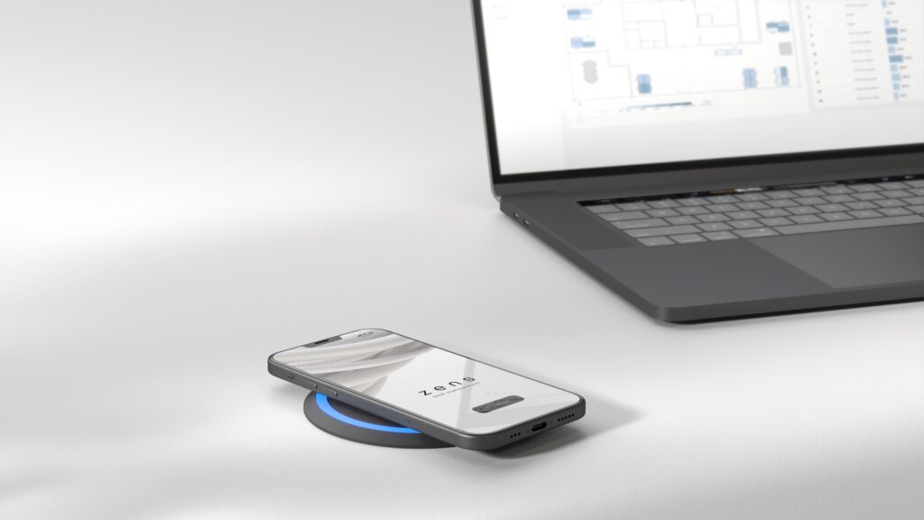 Wirelessly charging a mobile phone using the Zens Smart PuK and a laptop displaying desk booking management software.